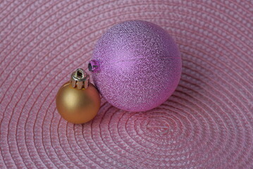 two glass purple and brown Christmas balls lie on a pink table