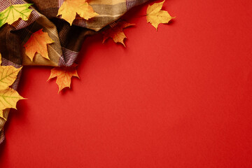 Hygge style plaid and maple leaves on red table. Autumn background. Flat lay, top view, copy space