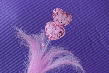 two small pink fabric hearts on a white plastic stick with feathers on a purple background