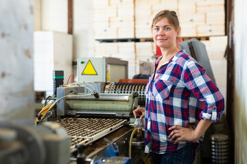 Confident woman machine operator working with automatic conveyor filling and seeding of plants in...