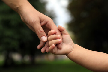 Daughter holding mother's hand in park, closeup. Happy family