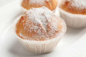 Tasty muffins powdered with sugar on plate, closeup