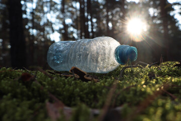 Used plastic bottle on grass in forest, closeup. Recycling problem