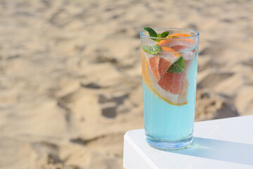 Glass of refreshing drink with grapefruit and mint on white table at beach, space for text