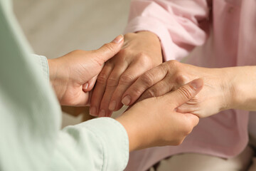 Fototapeta na wymiar Young and elderly women holding hands indoors, closeup