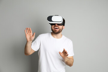 Happy man using virtual reality headset on light grey background