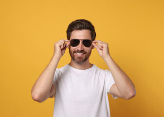 Portrait of smiling bearded man with stylish sunglasses on orange background