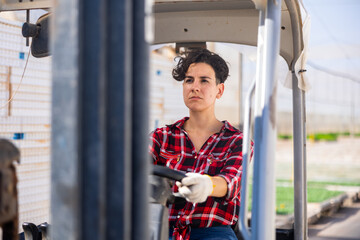 Concentrated woman working on forklift in large greenhouse