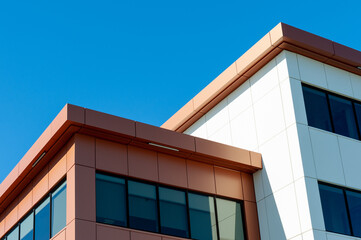 The roofs of a modern commercial building under blue sky and white clouds. The exterior of the new building is rusty, orange, and cream in color metal composite panels with black glass windows.   