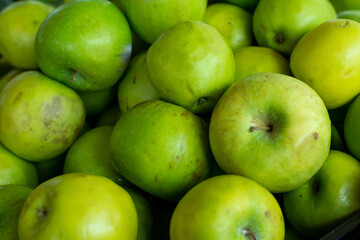 A stack or bulk supply of large vibrant green ripe Granny Smith apples on a table for sale at a farmer's market.  The sour organic apple has a tart flavor, firm texture, and green hue.