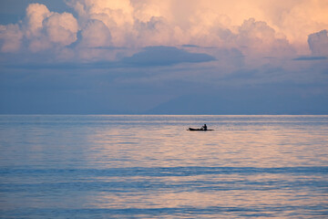 A local fishermen in a traditional wooden fishing canoe boat on the ocean with beautiful sunset reflecting pink hues over water on remote tropical Atauro Island, Timor Leste, Southeast Asia