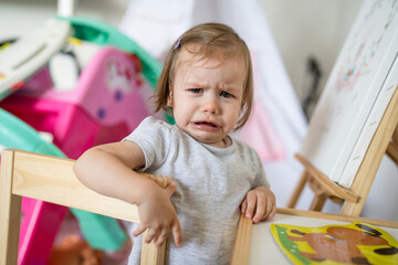 One child small caucasian girl toddler standing at home n room crying looking to the camera frustrated childhood unpleasant growing up concept copy space
