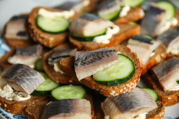 Defocus sandwich with herring and cucumber. A piece of black bread. Healthy food. Plate of sandwiches with fresh herring fish on dark background. Out of focus