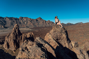 Girl sitting on the rocks in Teide National Park. Volcanic landscape. Roques de García trail. Tenerife, Canary islands, Spain.