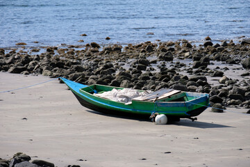 A traditional wooden fishing canoe boat resting on sandy rocky beach at low tide on remote tropical island in Southeast Asia