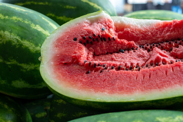 Fresh elongated watermelon with a transverse cut showing a pink chunky inside with lots of black...