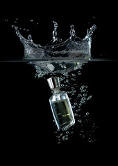 Bottle with perfume splashing into water on black background