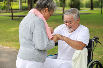 Obraz premium Asian senior woman or caregiver helping and consoling senior man walk with wheelchair at park outdoor. Elderly wife taking good help care and support of elder husband patient outside the house.