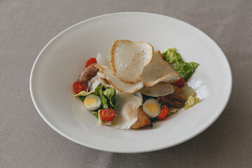 Caesar salad with roasted chicken breast, croutons, cherry tomatoes and parmesan on white plate
