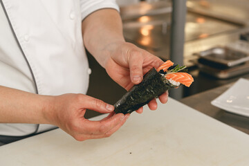 Chef hands cooking sushi with rice, salmon and nori on kitchen of japanese restaurant - obrazy, fototapety, plakaty