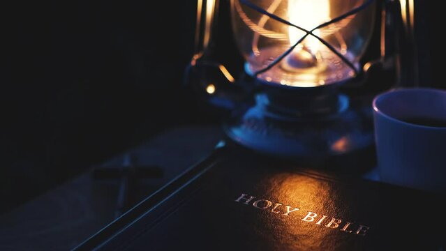 In the dark night, the relaxing sound of insects, the burning lamp, and the brightly shining holy bible and the cross of Jesus
