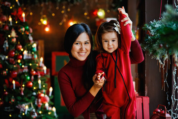 Happy mother and daughter pose in front of the Christmas tree. Beautiful stylish classic Christmas decorations. The concept of motherhood and childhood