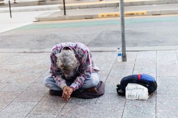 Anonymous homeless man on the street hanging his head obscuring his face in shame while begging for...