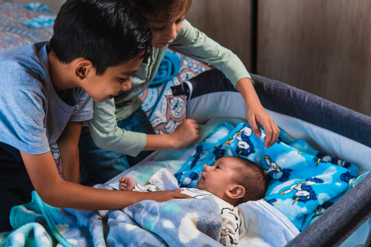 High quality photography. Multiracial Hispanic and American children with a newborn baby. Three brothers together in a room with a baby in the crib.