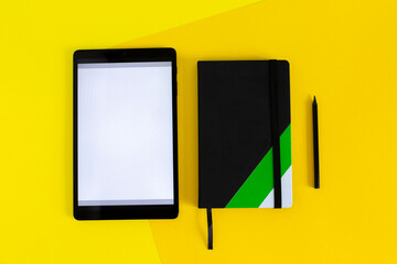 Home office flat lay with tablet and black notebook on yellow background