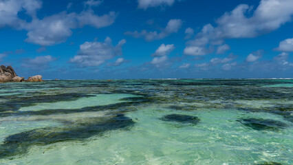 Tropical seascape. Clear transparent turquoise water and blue sky with cumulus clouds. Picturesque boulders are visible in the distance. Seychelles. La Digue. Anse Source D'Argent Beach