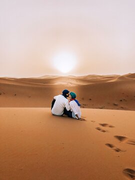 Back view of man and woman kissing and sitting in Moroccan desert