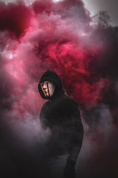 Man in white mask standing in the middle of red colored smoke