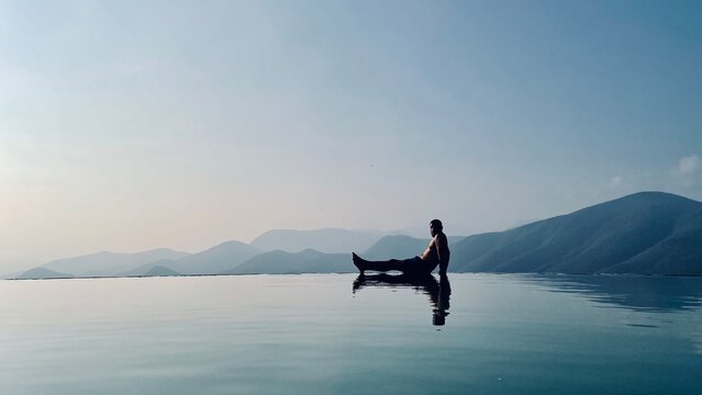 Man sitting on edge of infinity pool overlooking the mountains