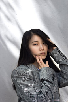 Portrait Of East Asian Woman In Gray Blazer Against Light Wall