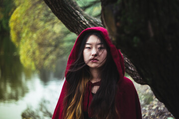 Portrait of young Asian looking woman in red cloak standing beside tree