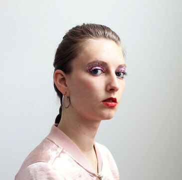 Portrait of young blonde woman with glitter eyeshadow against light backgound