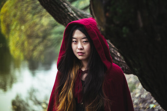 Portrait of young Asian looking woman in red cloak standing beside tree