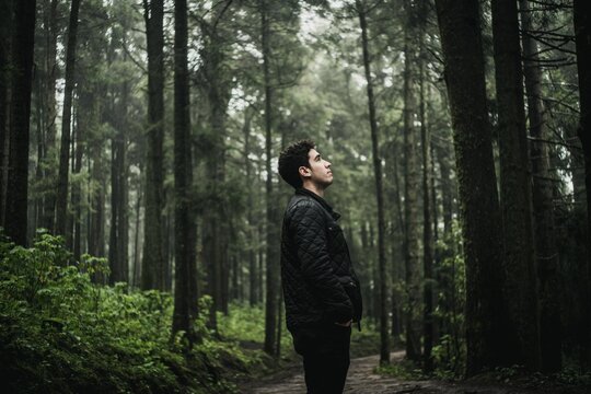 Side view of young man in leather jacket standing in the woods