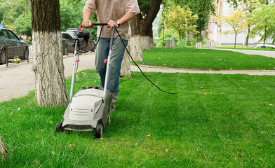 The worker cuts the high grass with an industrial electric lawn mower
