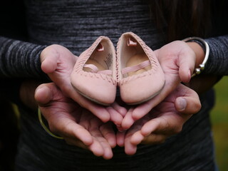 Two people holding pink baby girl shoes in their hands