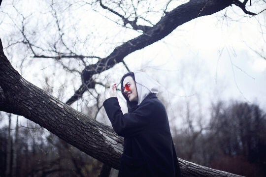 Woman in black coat holding black camera standing beside brown tree
