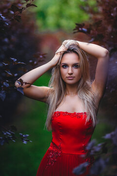 Woman wearing red strapless dress posing between trees