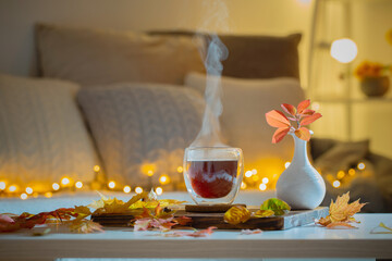 thermo glass with hot tea in dark night room with autumnal leaves