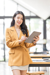 Successful Business Asian woman in Stylish Dress Using Tablet Computer, Standing in Modern Office...