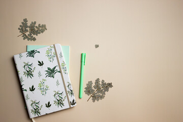 Notebook with mint pen and green leave on brown background. 