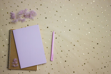 Purple notebooks with pen and flowers over the brown background. 