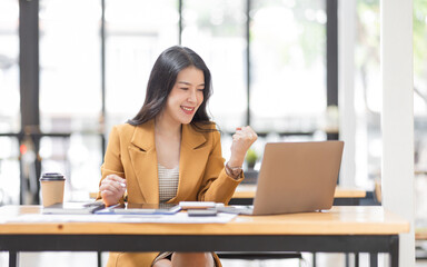 Successful Business Asian woman looks surprised and excited at laptop screen, receive pleasant notification, watching on laptop computer, cellular internet, Excited happy asian woman.