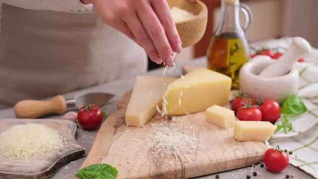 woman grates piece of parmesan hard cheese on a grater at domestic kitchen