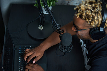 View from above of a black guy sitting at a laptop, talking into a microphone and reading the news....
