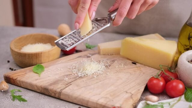 woman grates piece of parmesan hard cheese on a grater at domestic kitchen